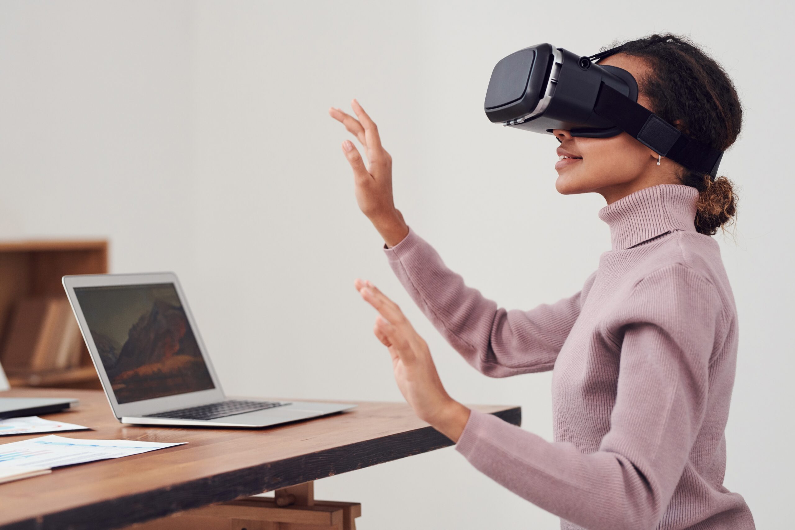 Met een VR bril stapt een vrouw je in een virtuele omgeving. Ze draagt hiervoor een VR-headset. Ze is aan het zitten en voor haar staat een laptop.